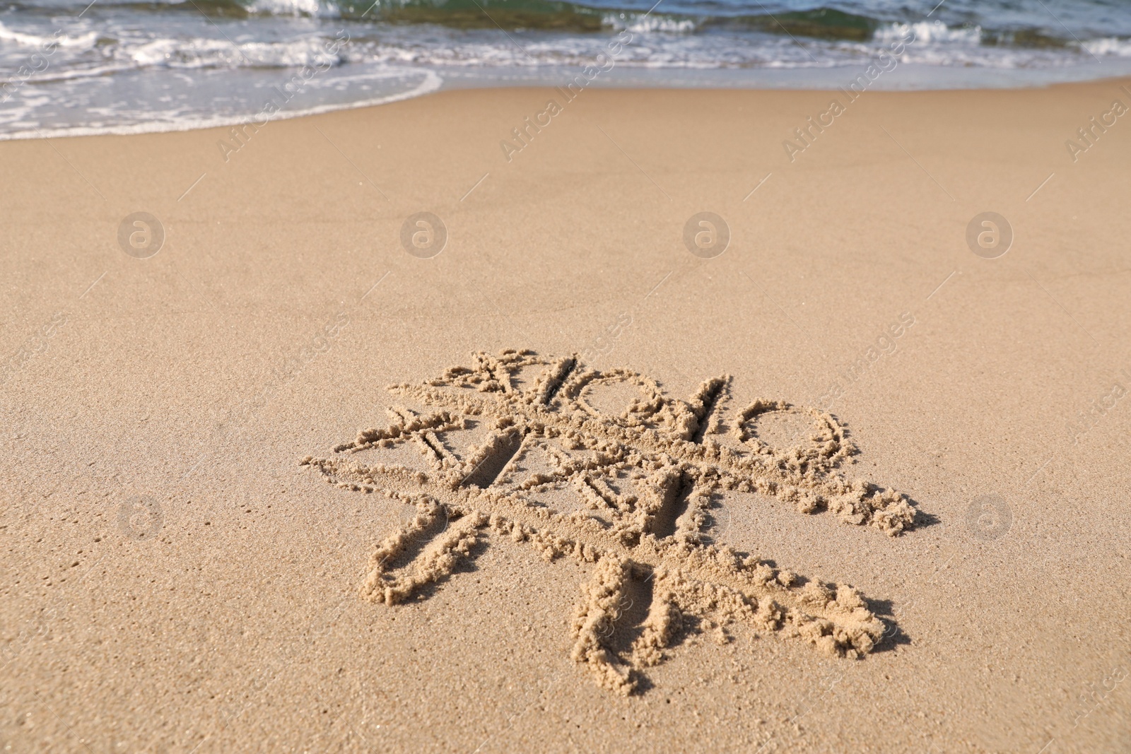 Photo of Tic tac toe game drawn on sand near sea, space for text