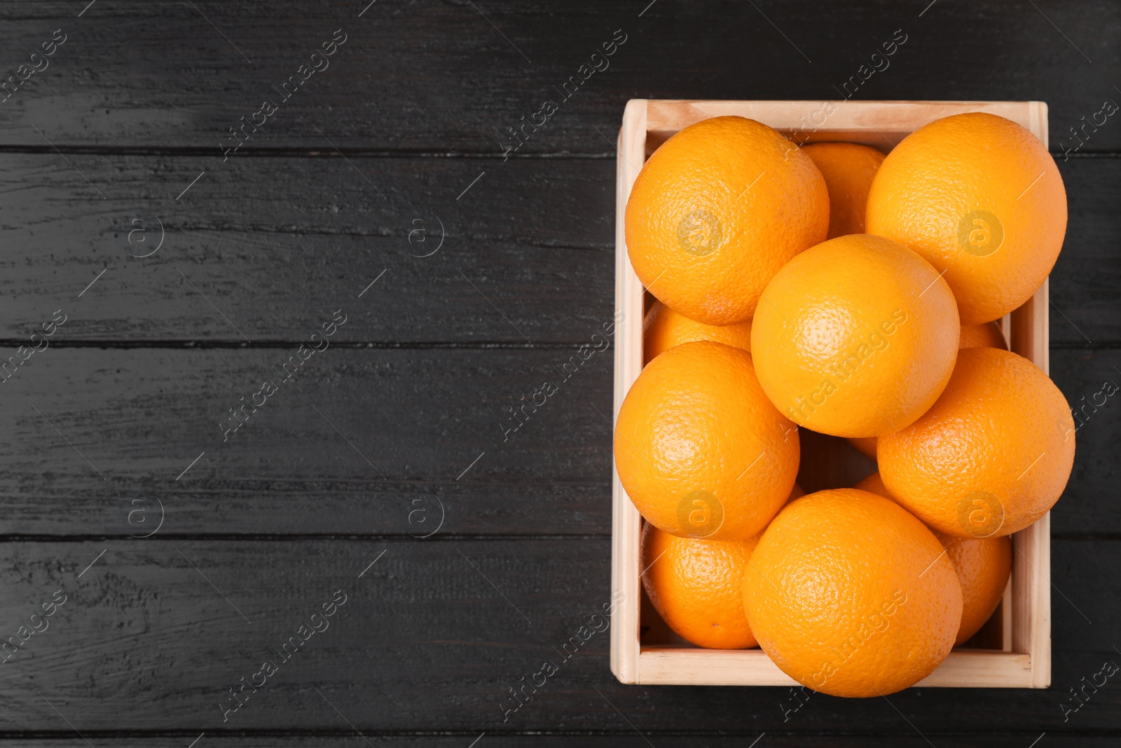 Photo of Wooden crate full of fresh oranges on dark background, top view. Space for text