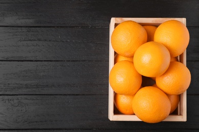 Wooden crate full of fresh oranges on dark background, top view. Space for text