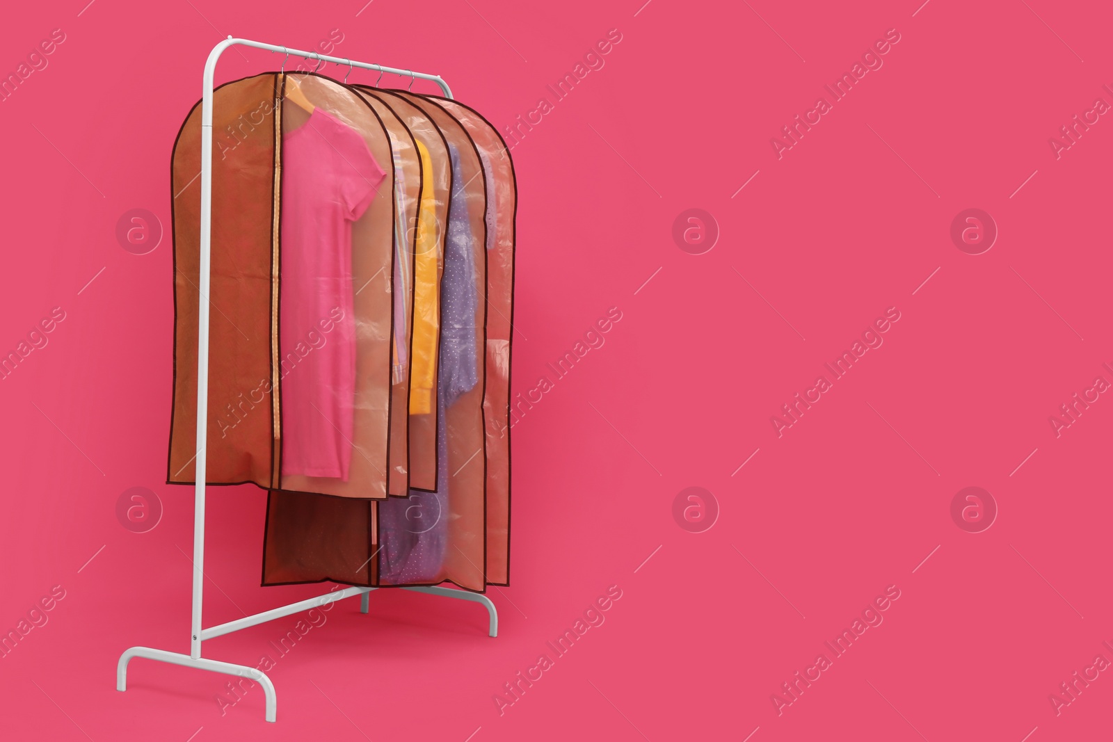 Photo of Garment bags with clothes on rack against pink background. Space for text