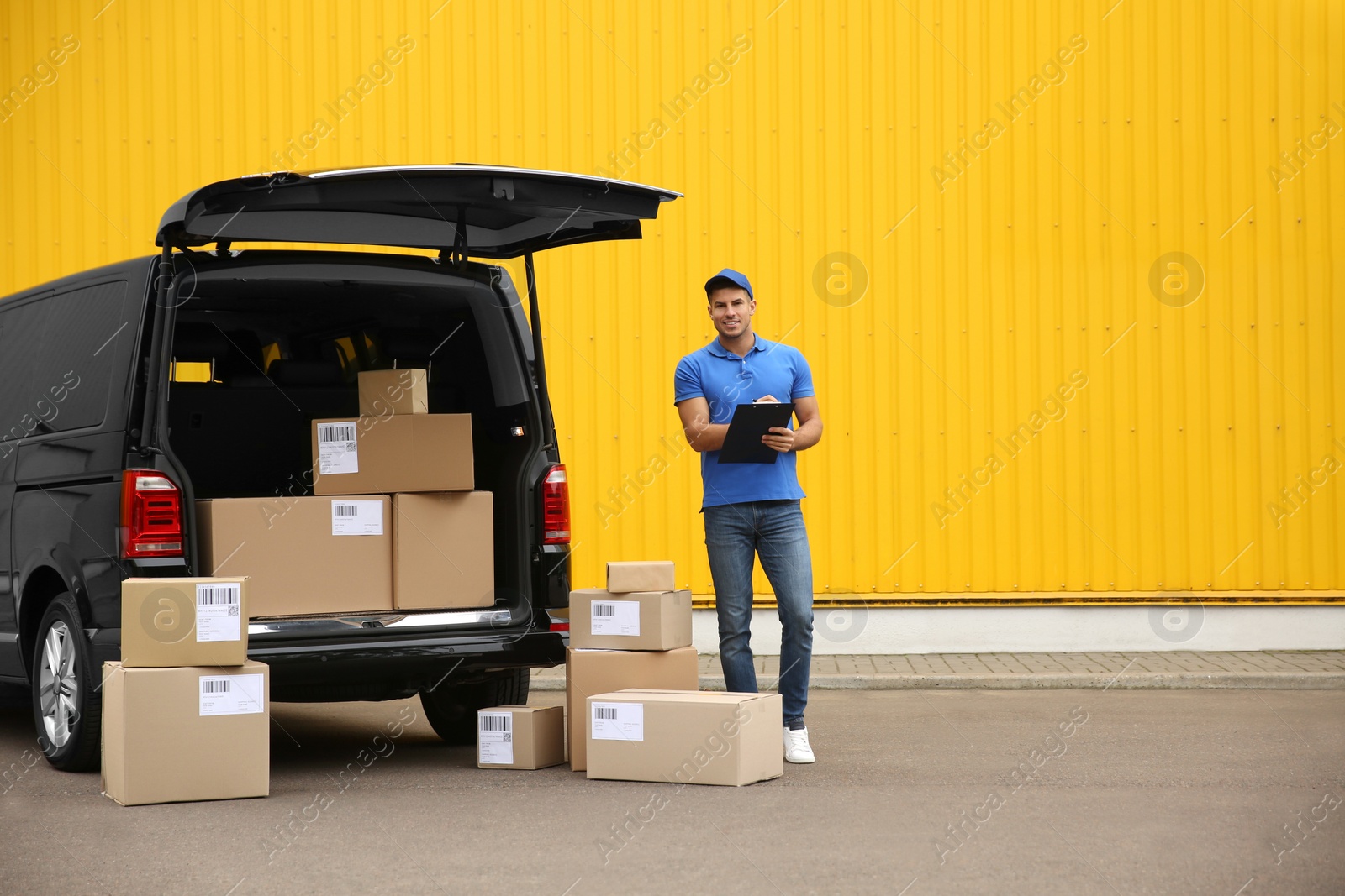 Photo of Courier with clipboard and parcels near delivery van outdoors