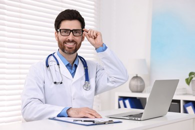 Photo of Medical consultant with glasses and stethoscope at table in clinic