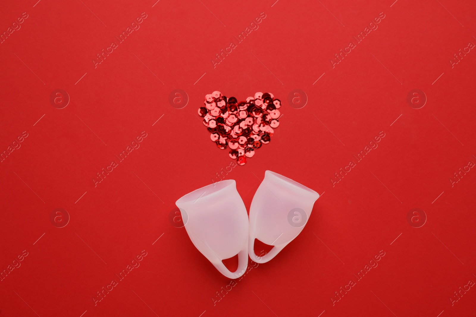 Photo of Menstrual cups near heart made of sequins on red background, flat lay