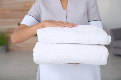 Photo of Young chambermaid with clean towels in hotel room, closeup