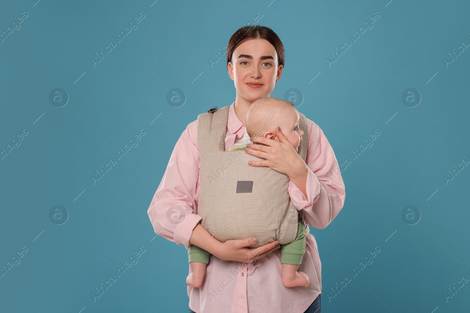 Photo of Mother holding her child in sling (baby carrier) on light blue background