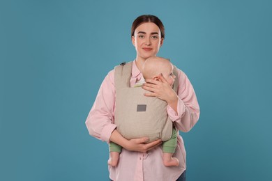 Mother holding her child in sling (baby carrier) on light blue background