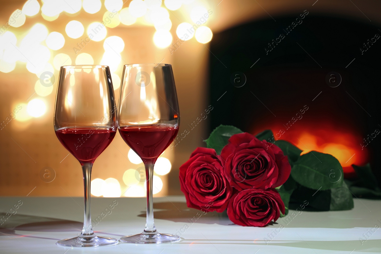 Photo of Glasses of wine and flowers on table against blurred lights. Romantic dinner