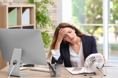 Photo of Businesswoman suffering from heat in front of small fan at workplace