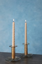 Photo of Holders with burning candles on black table near light blue wall
