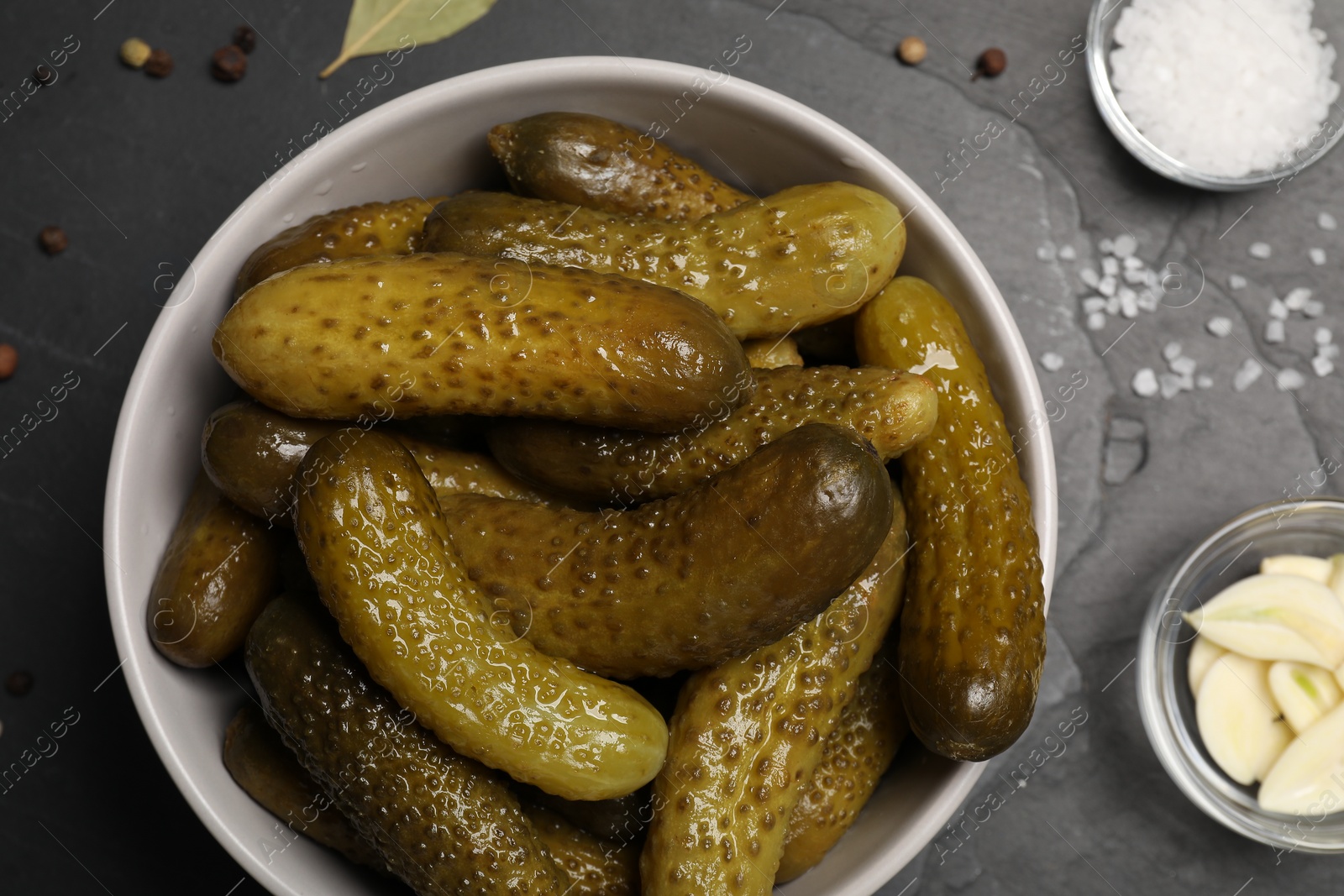 Photo of Tasty pickled cucumbers in bowl and spices on grey table, flat lay