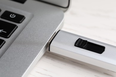 Photo of Modern usb flash drive attached into laptop on white wooden table, closeup