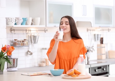 Beautiful young woman drinking milk in kitchen