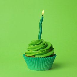 Photo of Delicious birthday cupcake with burning candle on green background