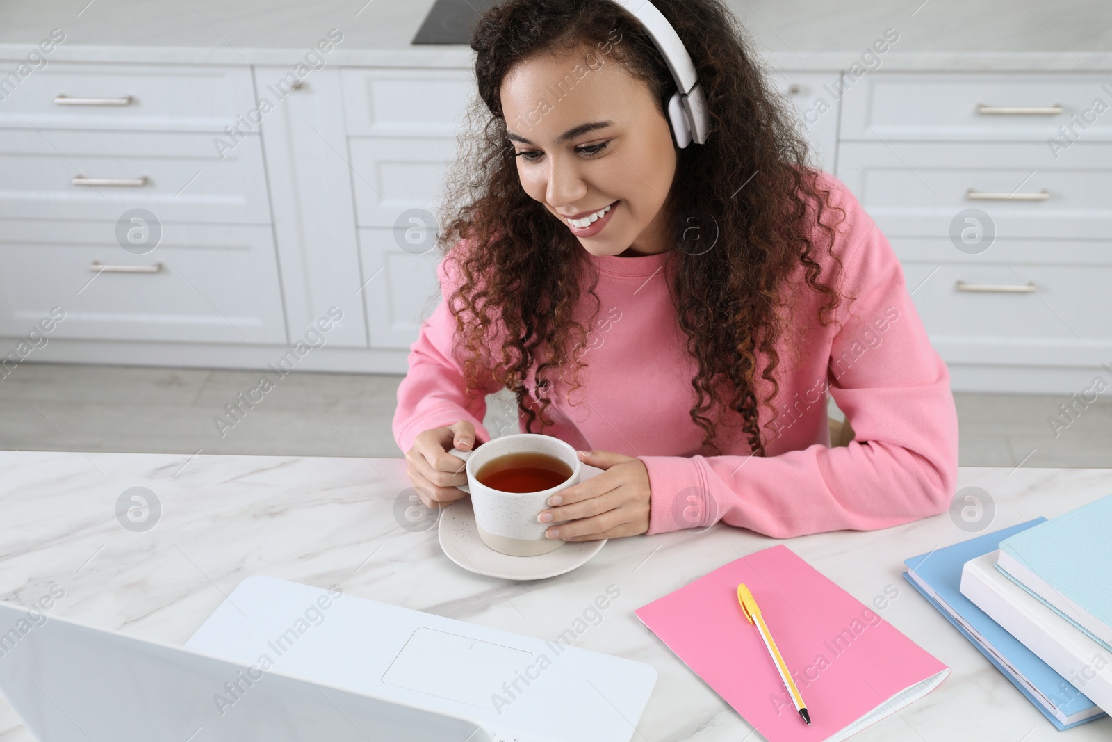 Photo of African American woman drinking tea while studying in kitchen at home. Distance learning