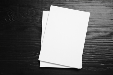 Stack of blank paper sheets for brochure on black wooden background, top view. Mock up