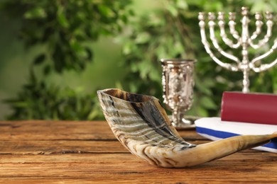 Photo of Shofar and other Rosh Hashanah holiday attributes on wooden table outdoors, space for text