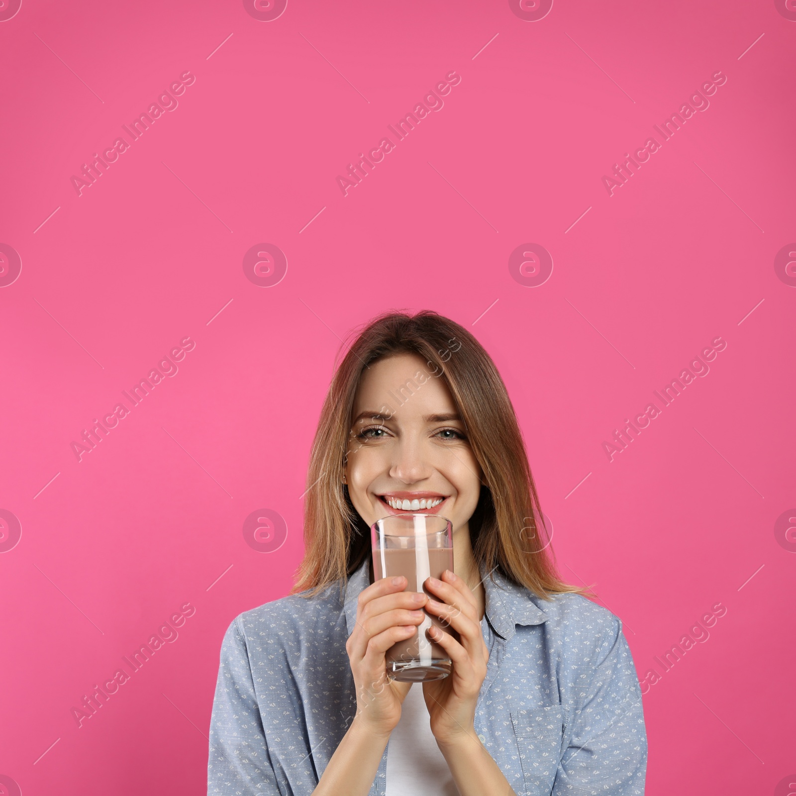 Photo of Young woman drinking chocolate milk on pink background