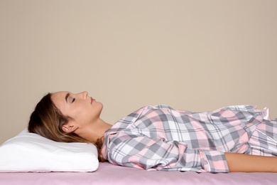 Photo of Beautiful teen girl sleeping with orthopedic pillow on bed against color background. Space for text