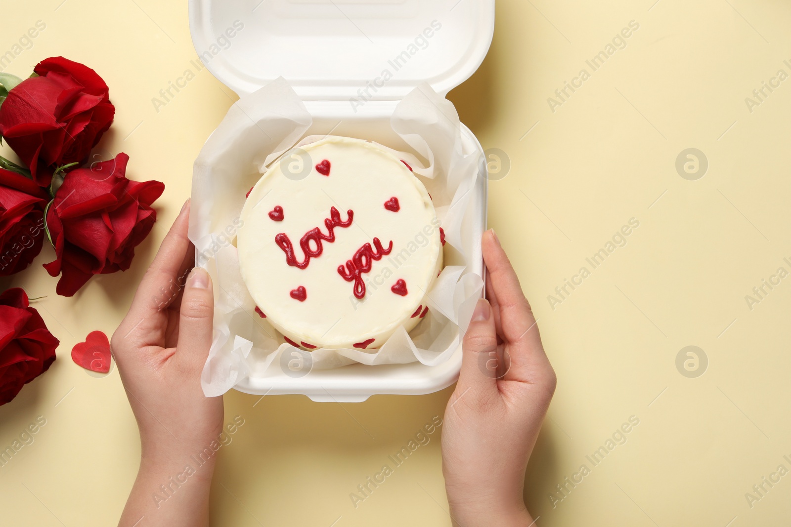 Photo of Woman holding takeaway box with bento cake at beige table, top view. St. Valentine's day surprise