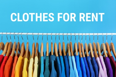 Rack with bright clothes for rent on light blue background
