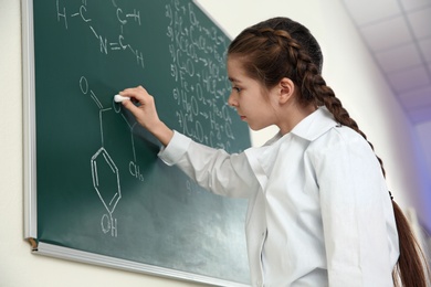 Schoolgirl writing chemistry formula on blackboard in class