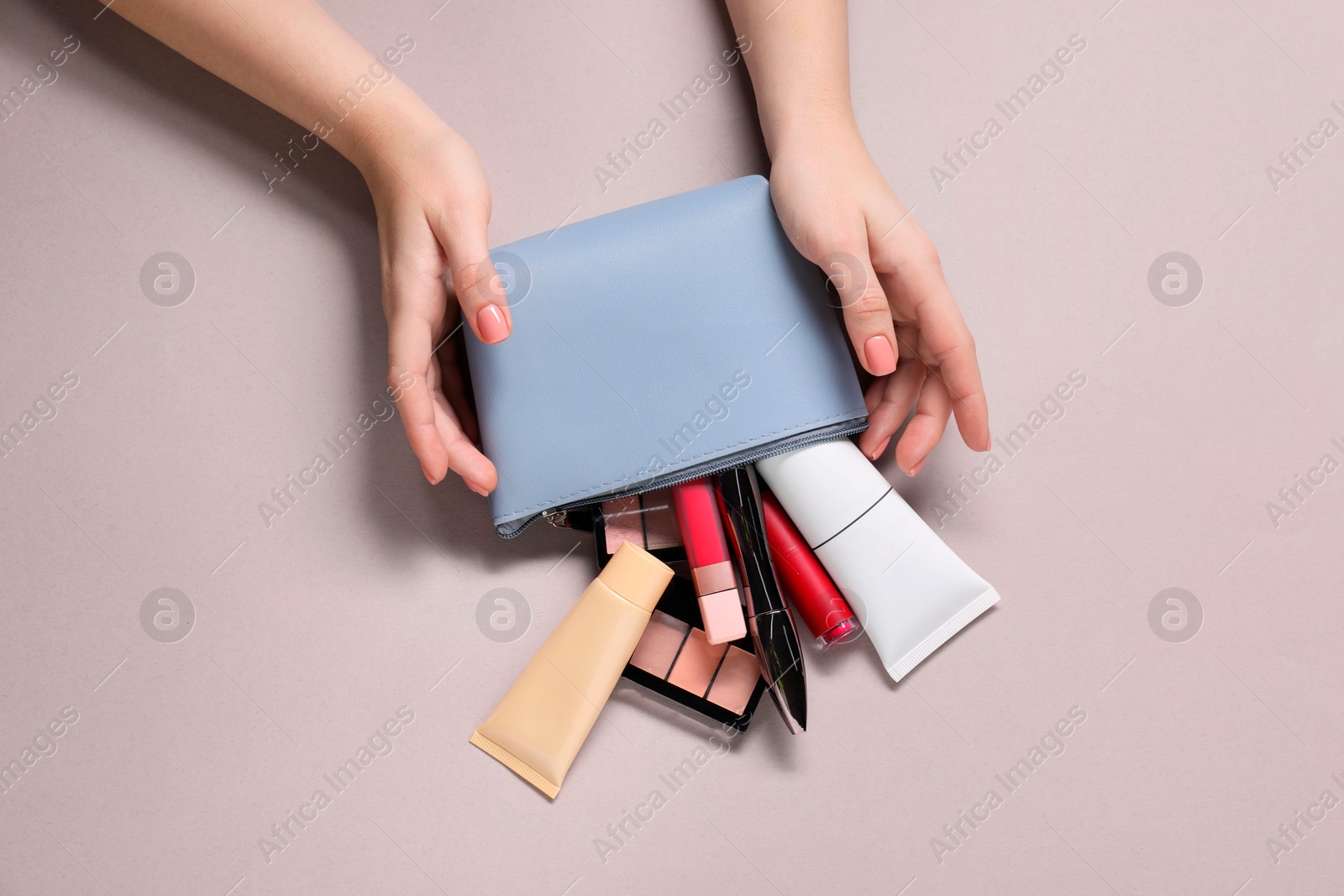 Photo of Woman with cosmetic bag and different makeup products on beige background, top view