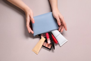 Woman with cosmetic bag and different makeup products on beige background, top view