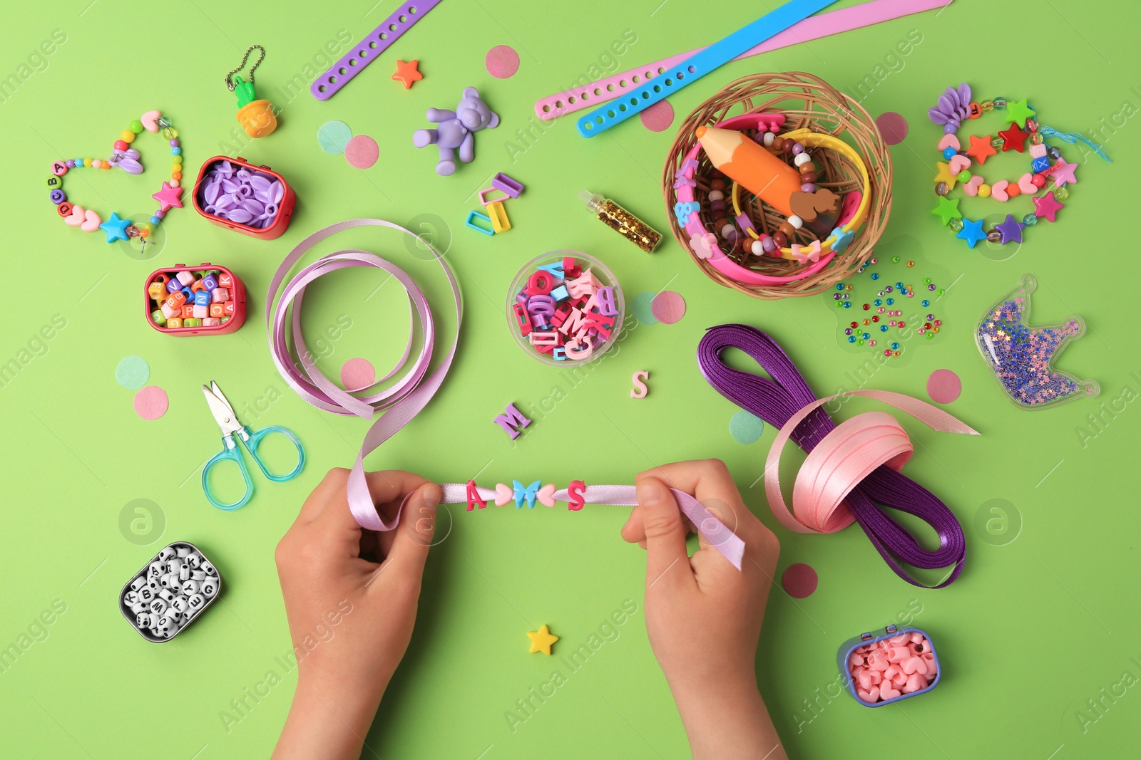 Photo of Child making beaded jewelry and different supplies on green background, top view. Handmade accessories