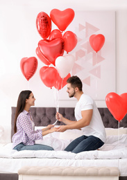 Photo of Romantic couple with heart shaped balloons in bedroom. Valentine's day celebration