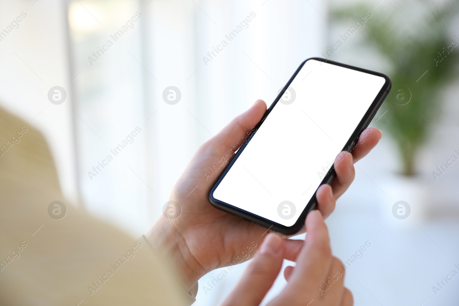 Image of Woman holding mobile phone with empty screen indoors, closeup