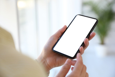 Image of Woman holding mobile phone with empty screen indoors, closeup