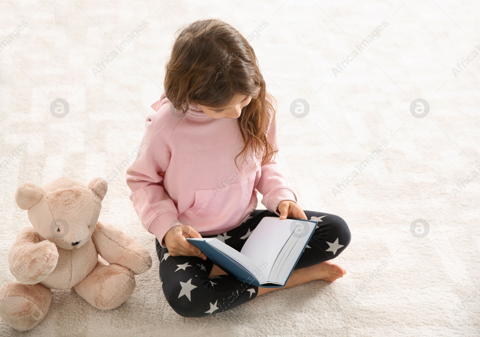 Photo of Cute little girl with teddy bear reading book on floor. Space for text