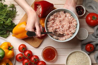 Woman making stuffed peppers with ground meat at white wooden table, top view