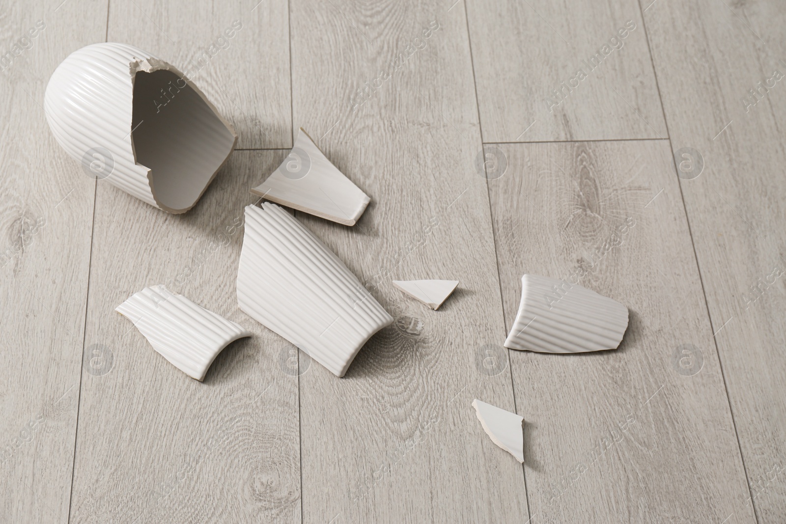 Photo of Broken white ceramic vase on wooden floor