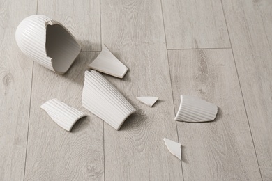 Broken white ceramic vase on wooden floor