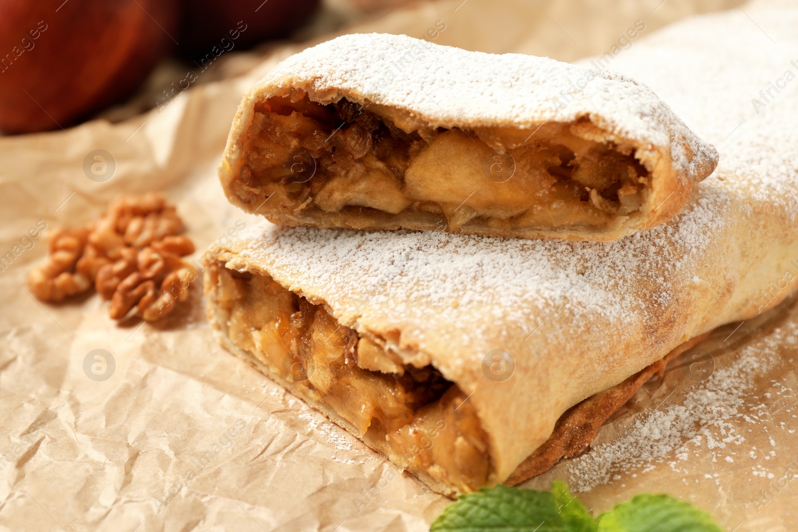 Photo of Delicious apple strudel with walnuts and powdered sugar on parchment paper, closeup