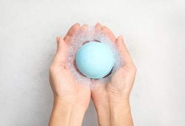 Photo of Woman holding color bath bomb over foam, top view