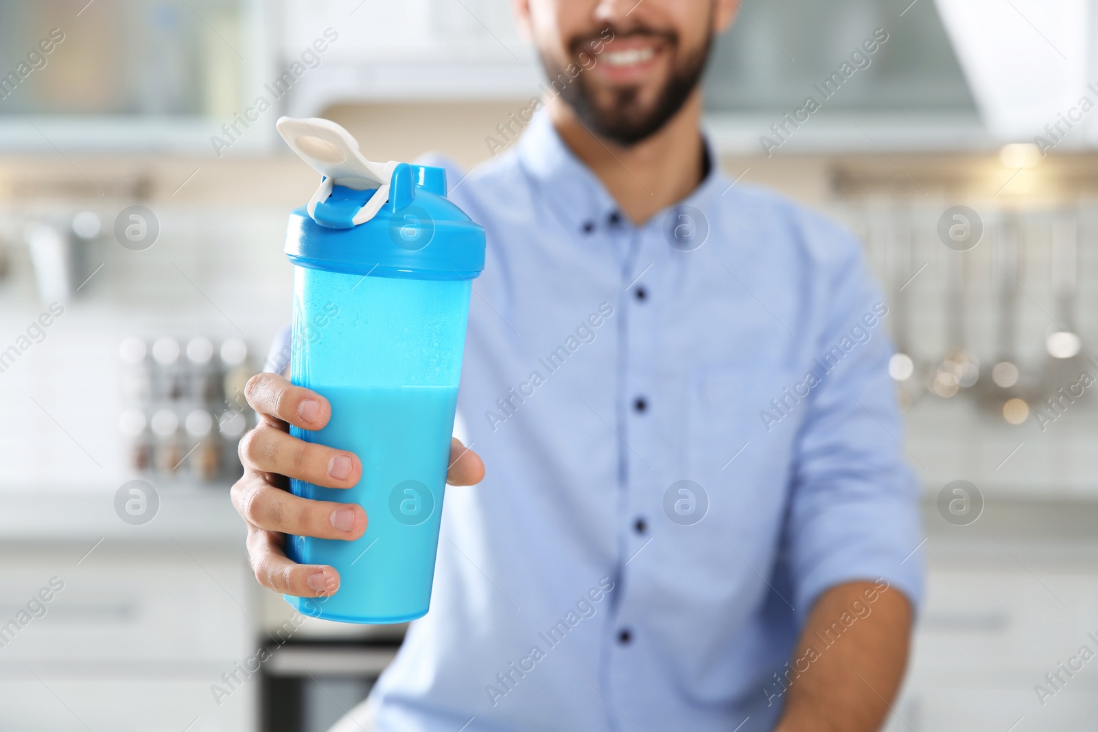 Photo of Young man holding bottle of protein shake in kitchen, closeup