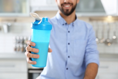 Young man holding bottle of protein shake in kitchen, closeup