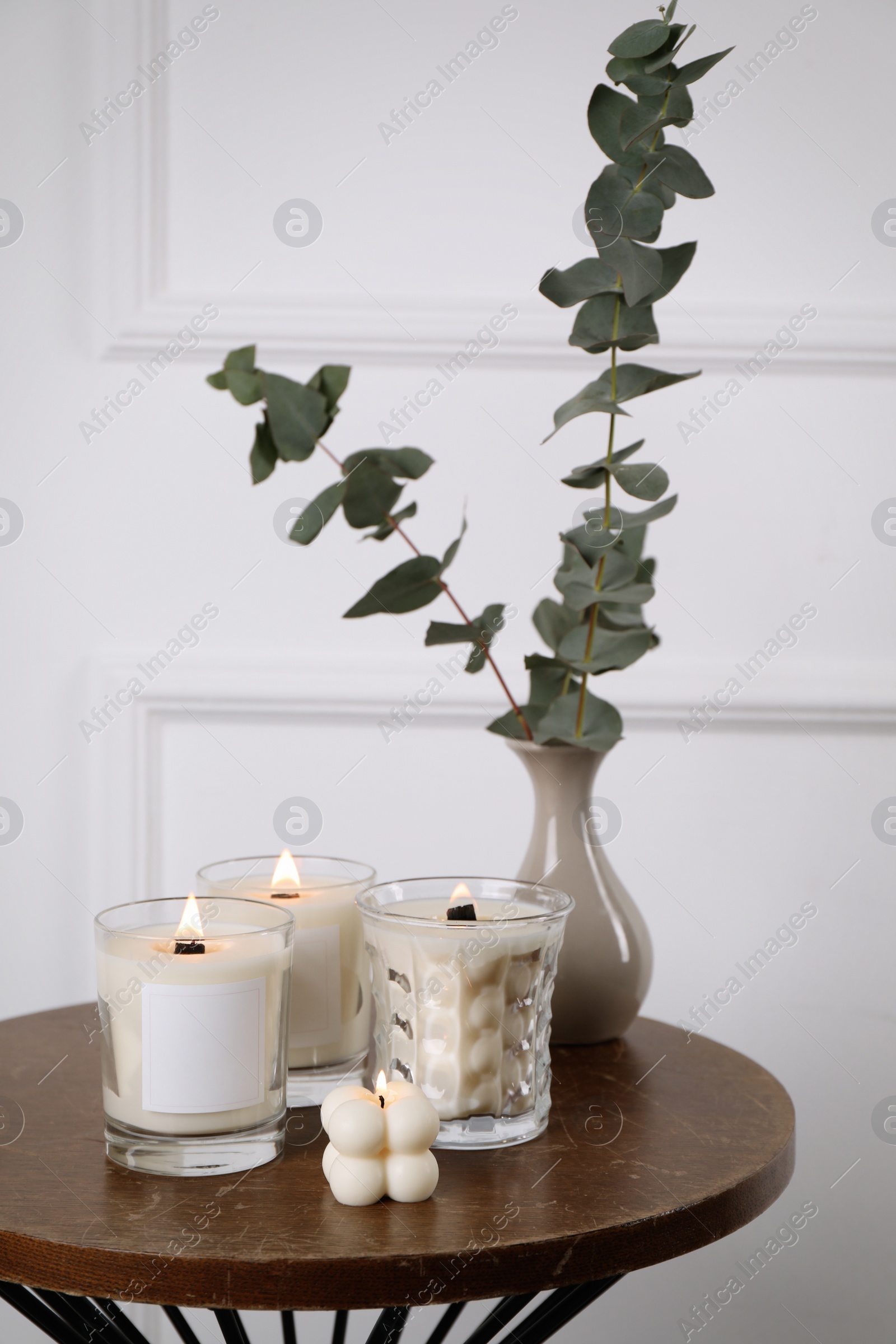 Photo of Different soy candles and eucalyptus on wooden table indoors