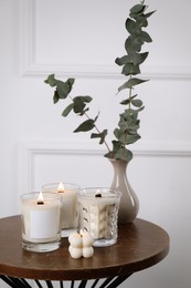 Different soy candles and eucalyptus on wooden table indoors