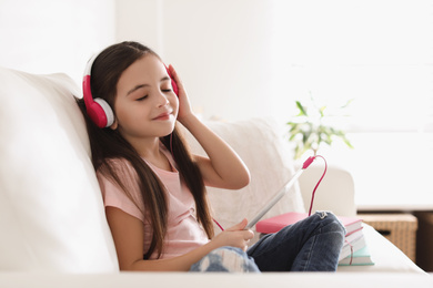 Cute little girl with headphones and tablet listening to audiobook at home