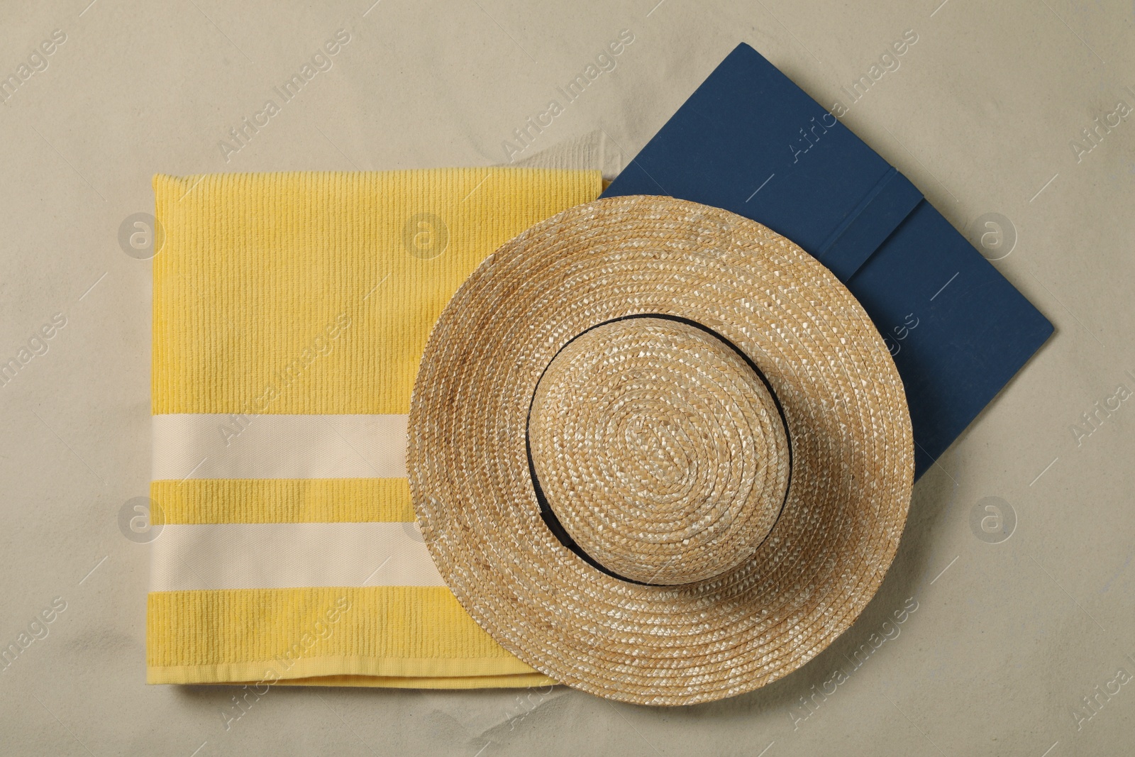 Photo of Beach towel, hat and book on sand, top view