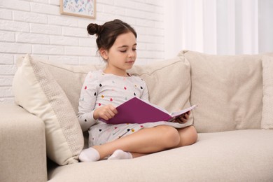 Photo of Little girl reading book on sofa at home