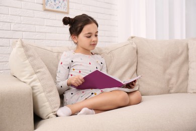 Little girl reading book on sofa at home