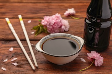 Photo of Bottle, bowl with soy sauce, chopsticks and flowers on wooden table