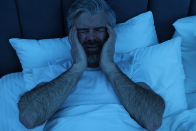 Mature man suffering from headache in bed at night