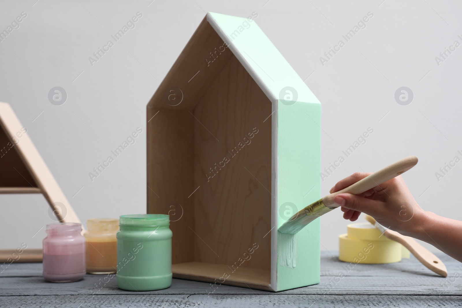 Photo of Woman painting wooden house model at grey table, closeup