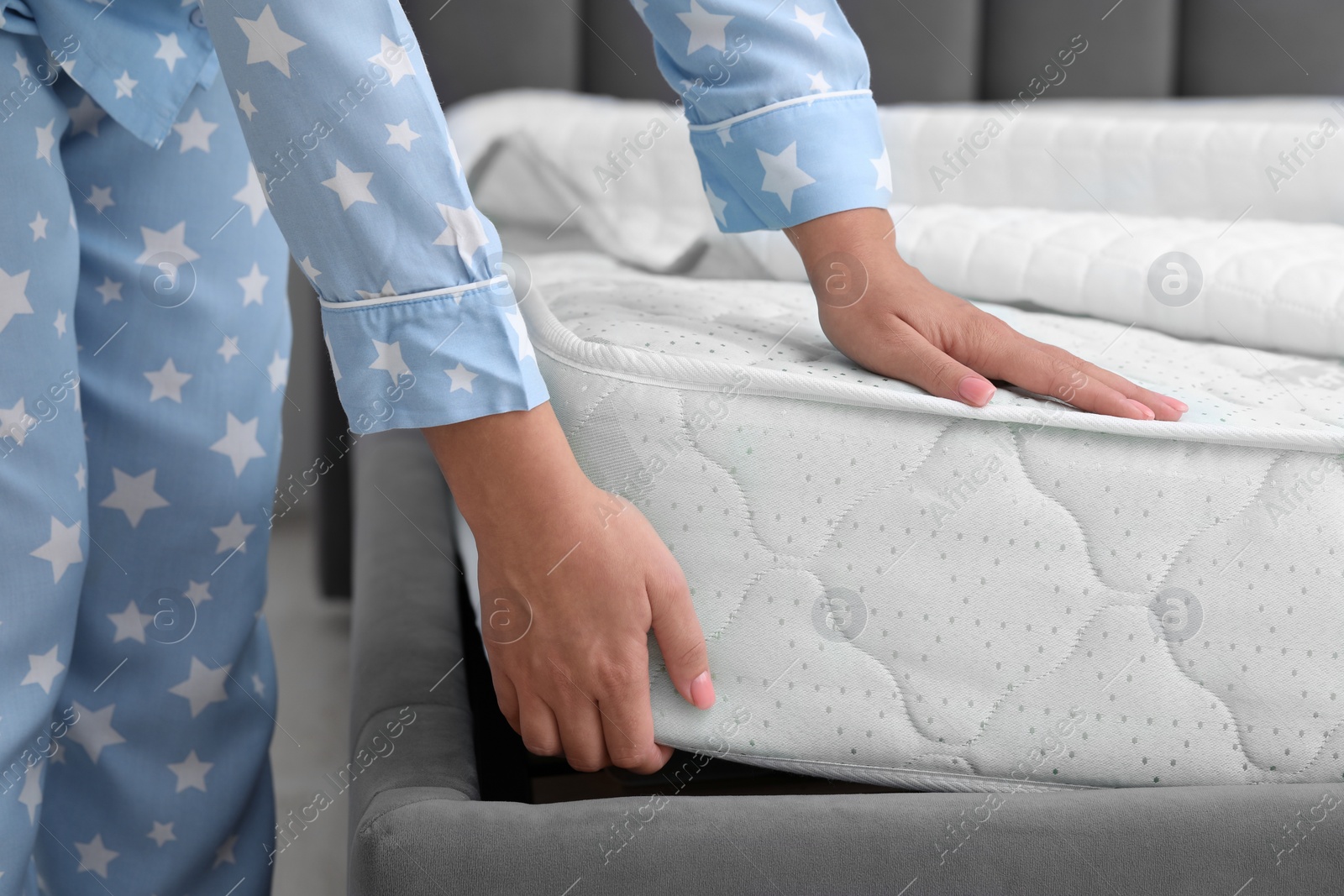 Photo of Woman putting new soft mattress on grey bed indoors, closeup