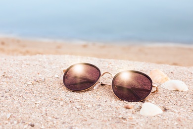 Photo of Stylish sunglasses and shells on sandy beach near sea